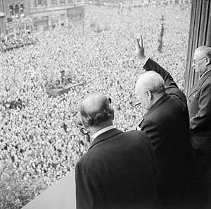 Winston Churchill waves to crowds in Whitehall in London as they celebrate VE Day, 8 May 1945. H41849.jpg