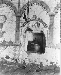 (PD) Photo: Charles C. Pierce An ancient baptismal font at the San Antonio de Pala Asistencia, circa 1900. The font resides in a groove cut into the wall; the pictures painted on the wall depict gravestones, a book, an arch, and corridor arches.