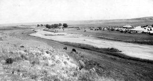 (PD) Photo: Earl Alonzo Brininstool A view of tents, buildings, horses, and cattle at the annual scout reunion in 1917 to commemorate the Battle of Beecher Island near Wray, in Yuma County, Colorado. The Arickaree River flows near the camp. The Battle of Beecher Island monument is visible in the distance.